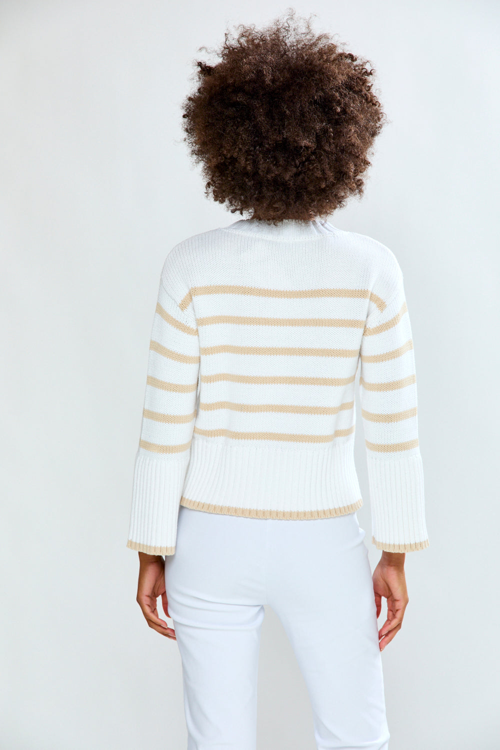 Person wearing a white sweater with gold stripes on a plain background
