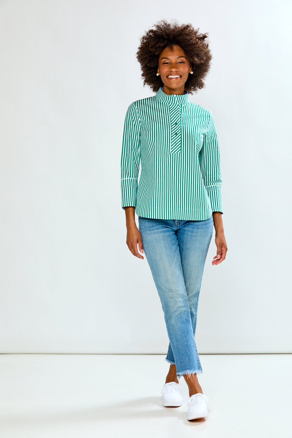 Woman wearing a green and white striped shirt with blue jeans on a white background