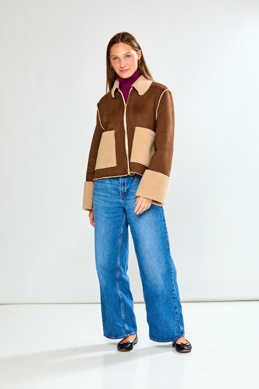 Woman wearing a brown and beige jacket with blue jeans on a white background