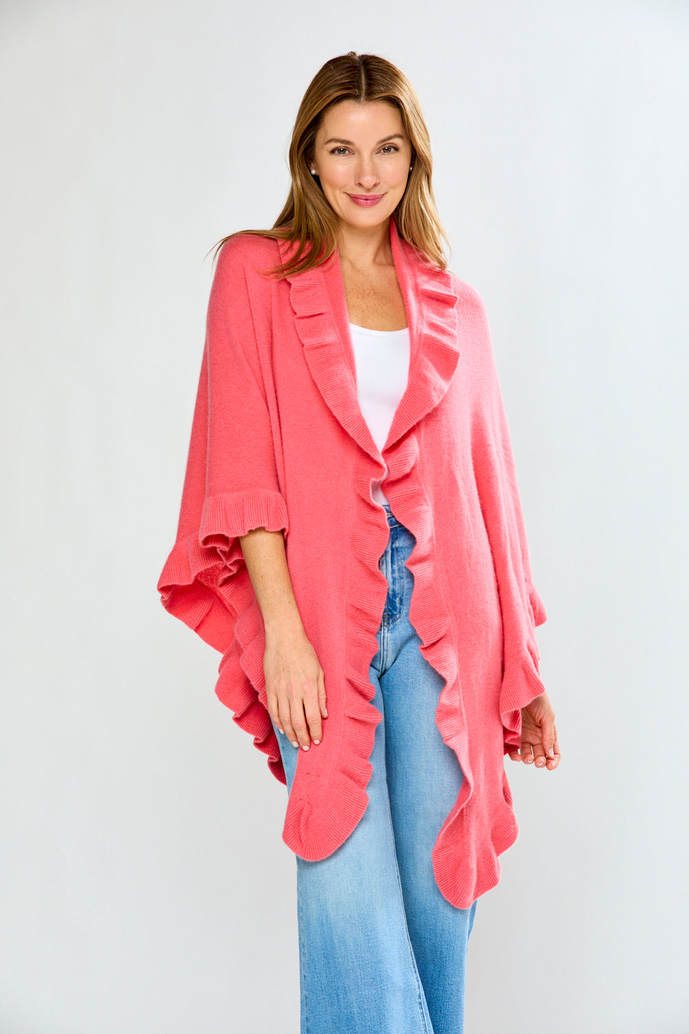 Woman wearing a pink cardigan over a white top and blue jeans on a light gray background