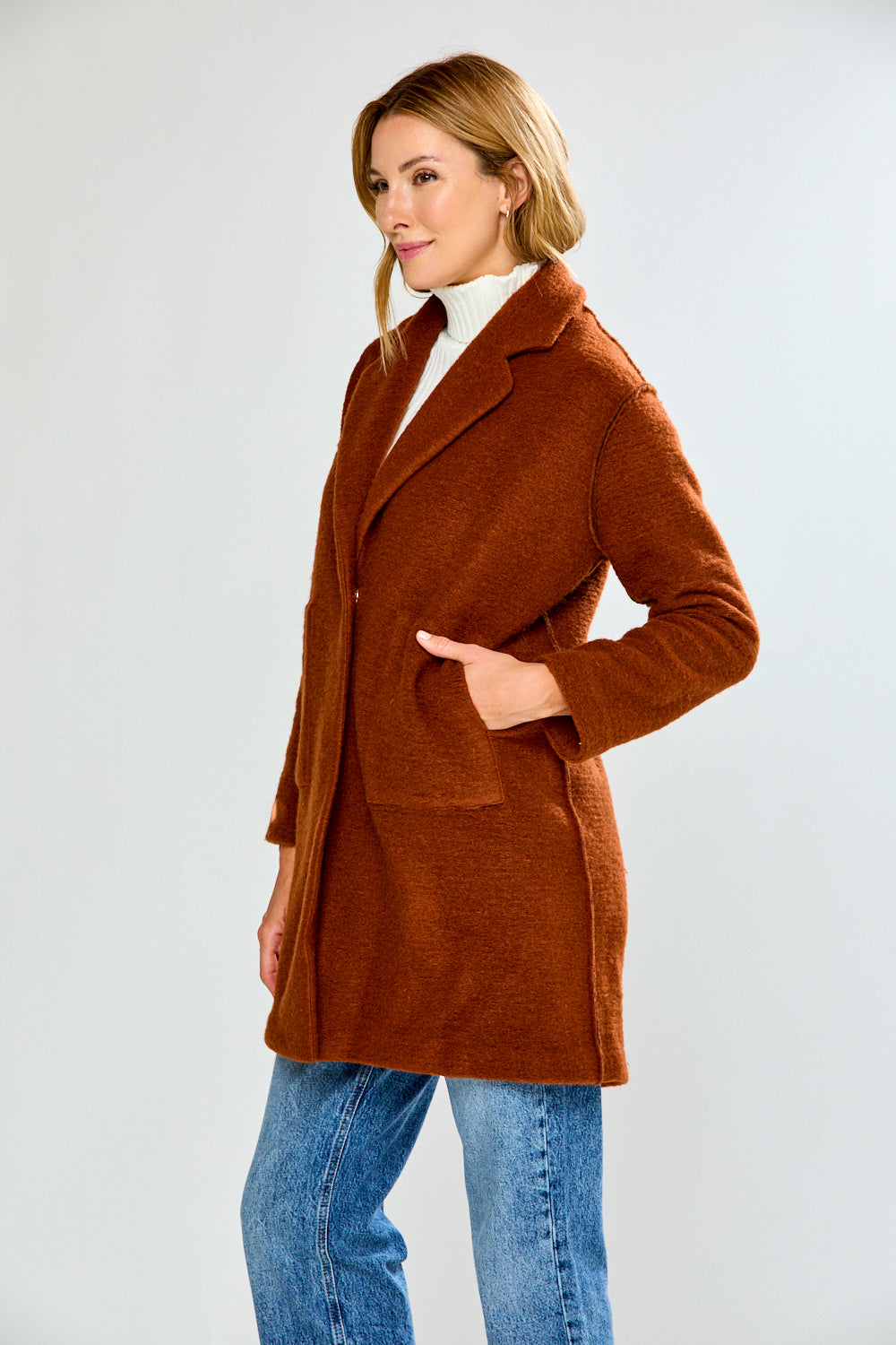 Woman wearing a brown coat over a white turtleneck on a white background