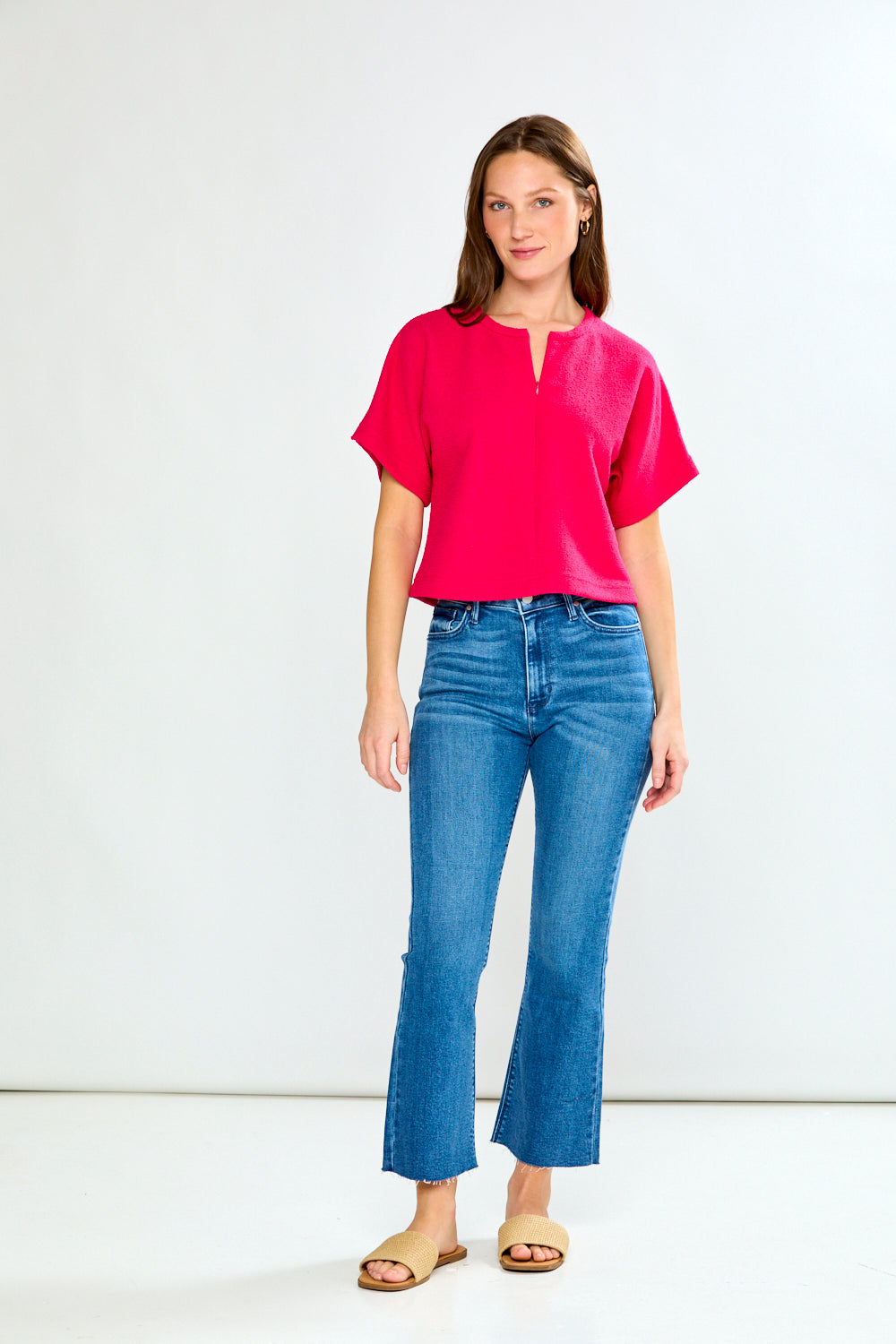 Woman wearing a bright pink top and blue jeans on a white background
