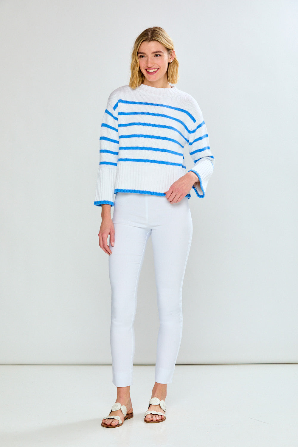 Woman wearing a white and blue striped sweater with white pants on a white background
