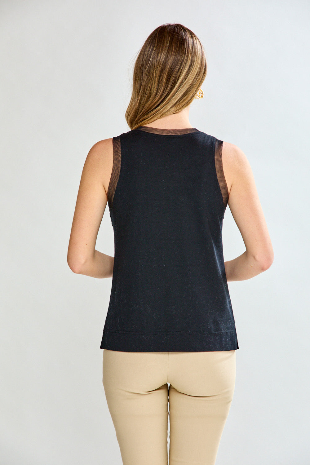 Woman wearing a black sleeveless top with sheer mesh details on a plain background