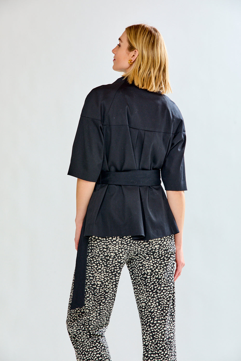 Woman wearing a black belted jacket and patterned pants on a white background