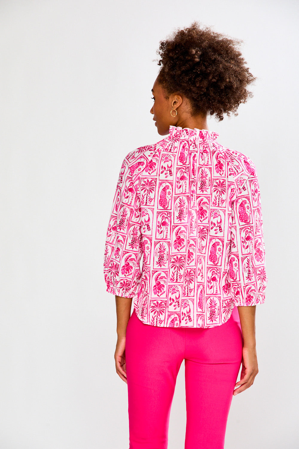 Woman wearing a pink patterned blouse and pink pants on a white background
