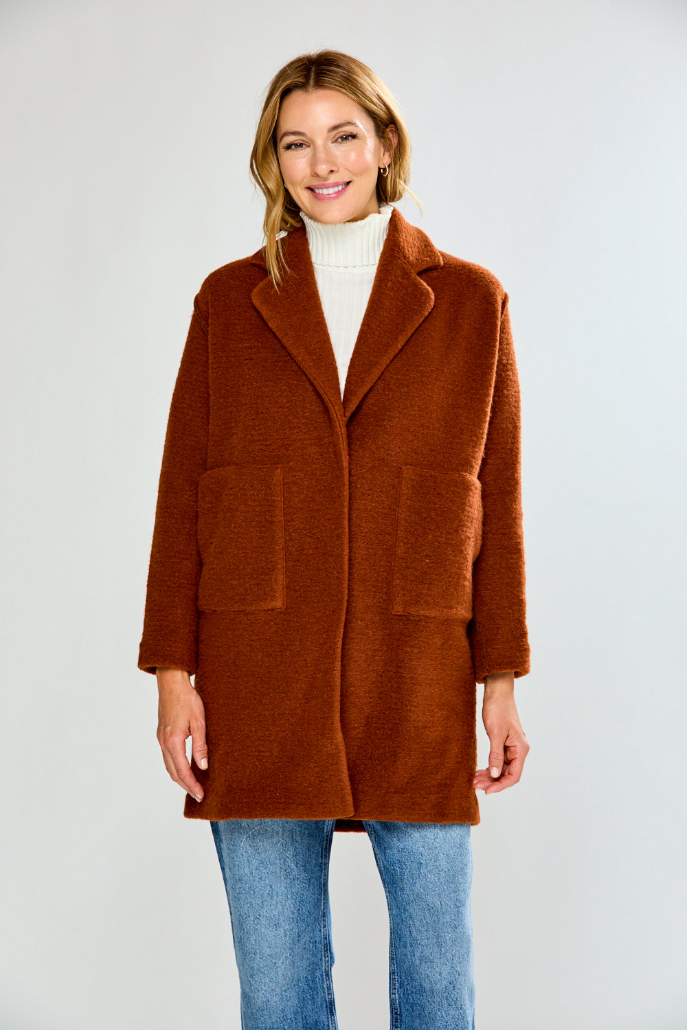 Woman wearing a brown coat over a white turtleneck on a white background