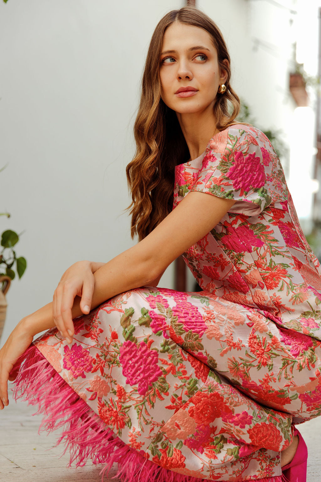 Woman wearing a pink floral dress with fringe sitting on a wooden floor.