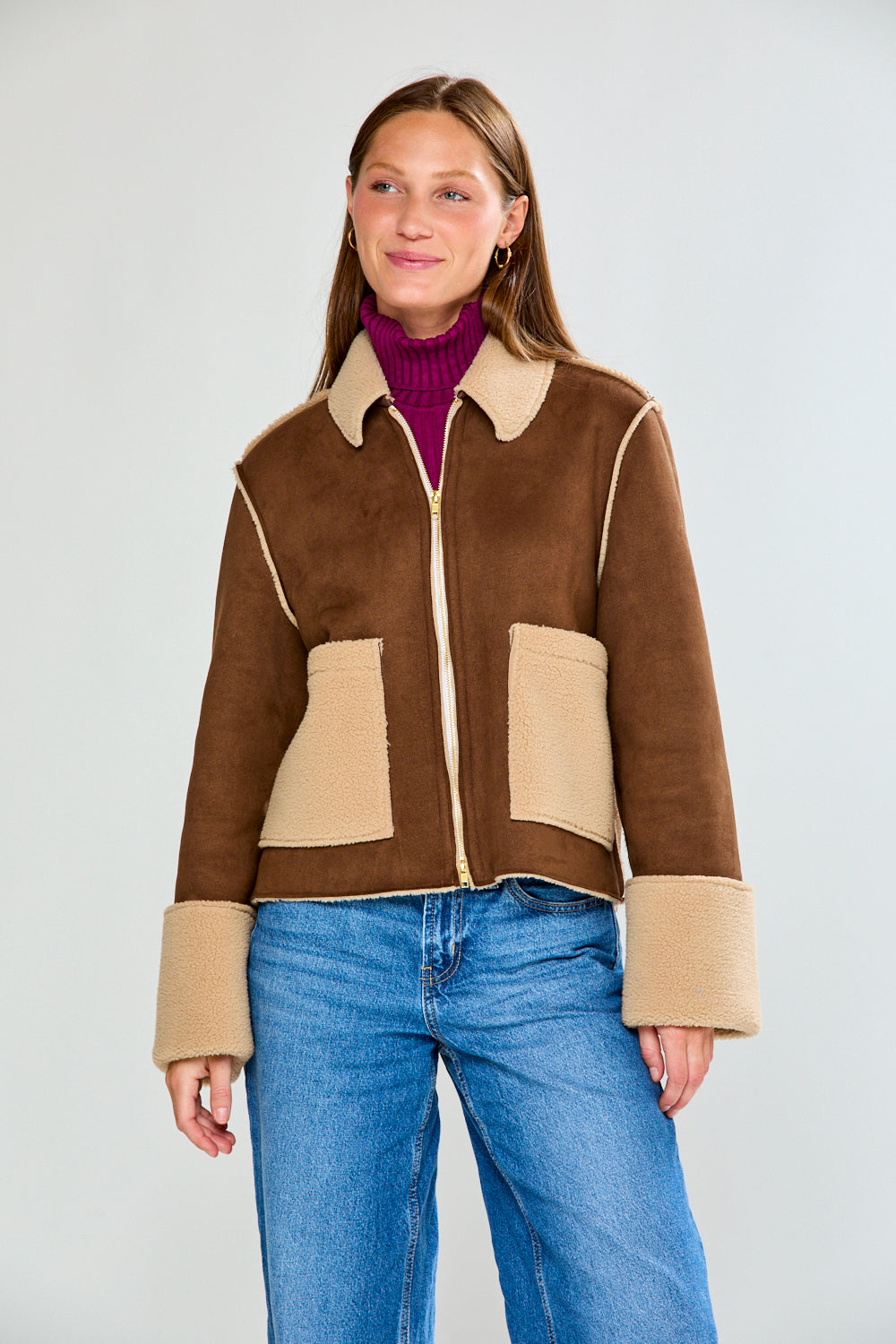 Woman wearing a brown and beige jacket with blue jeans on a white background