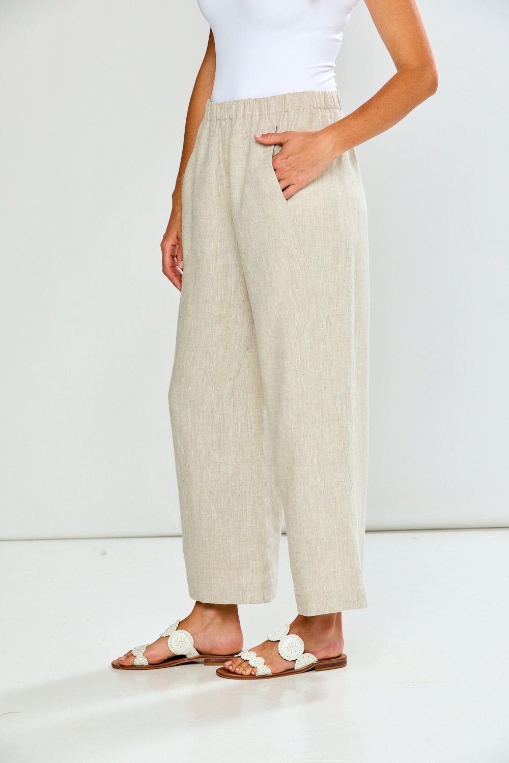 Person wearing beige pants and white sandals on a plain background