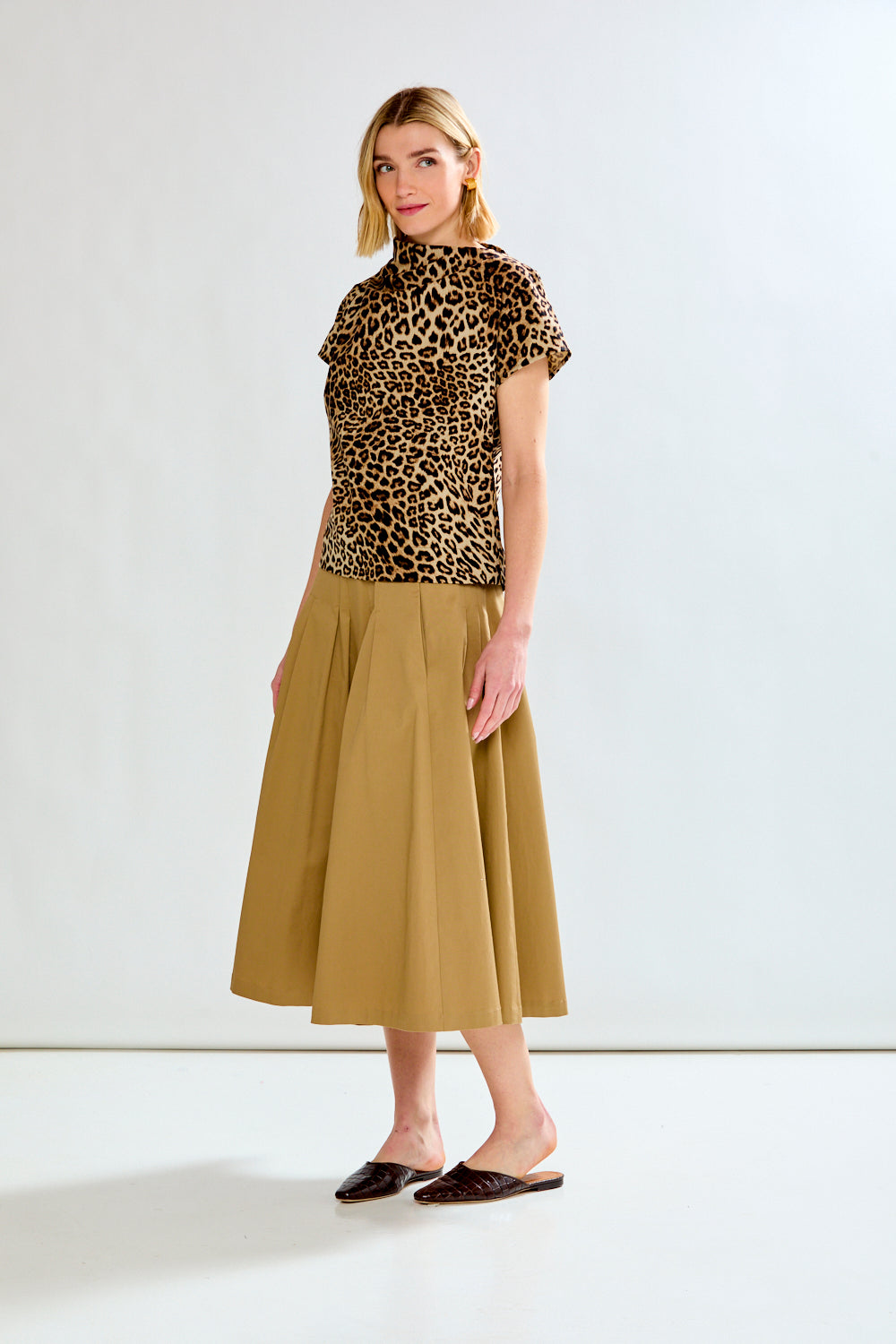 Woman wearing a leopard print top and beige skirt on a white background