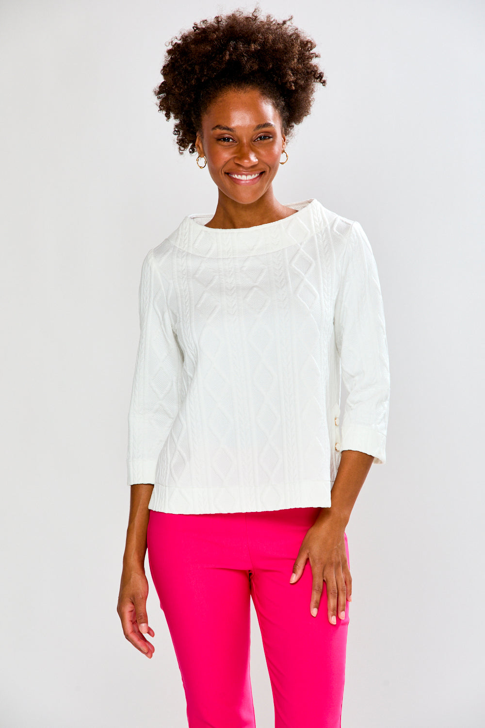 Woman wearing a white top and pink pants on a plain background