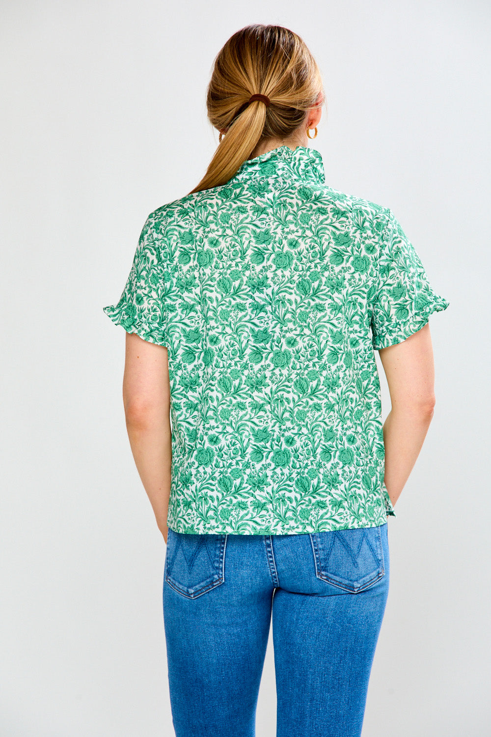 Person wearing a green floral shirt and blue jeans on a white background
