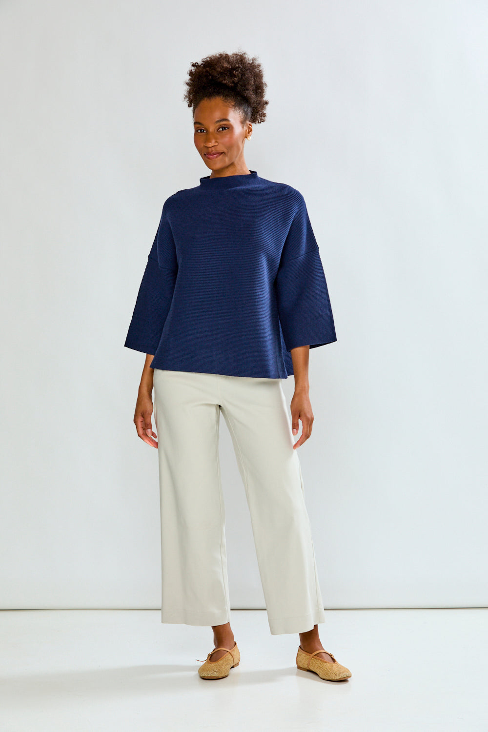 Person wearing a navy blue top and white pants on a white background