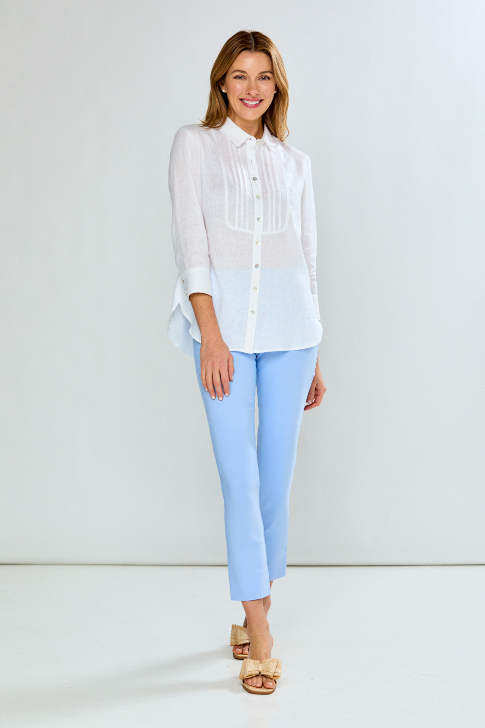 Woman wearing a white blouse and light blue pants against a white background