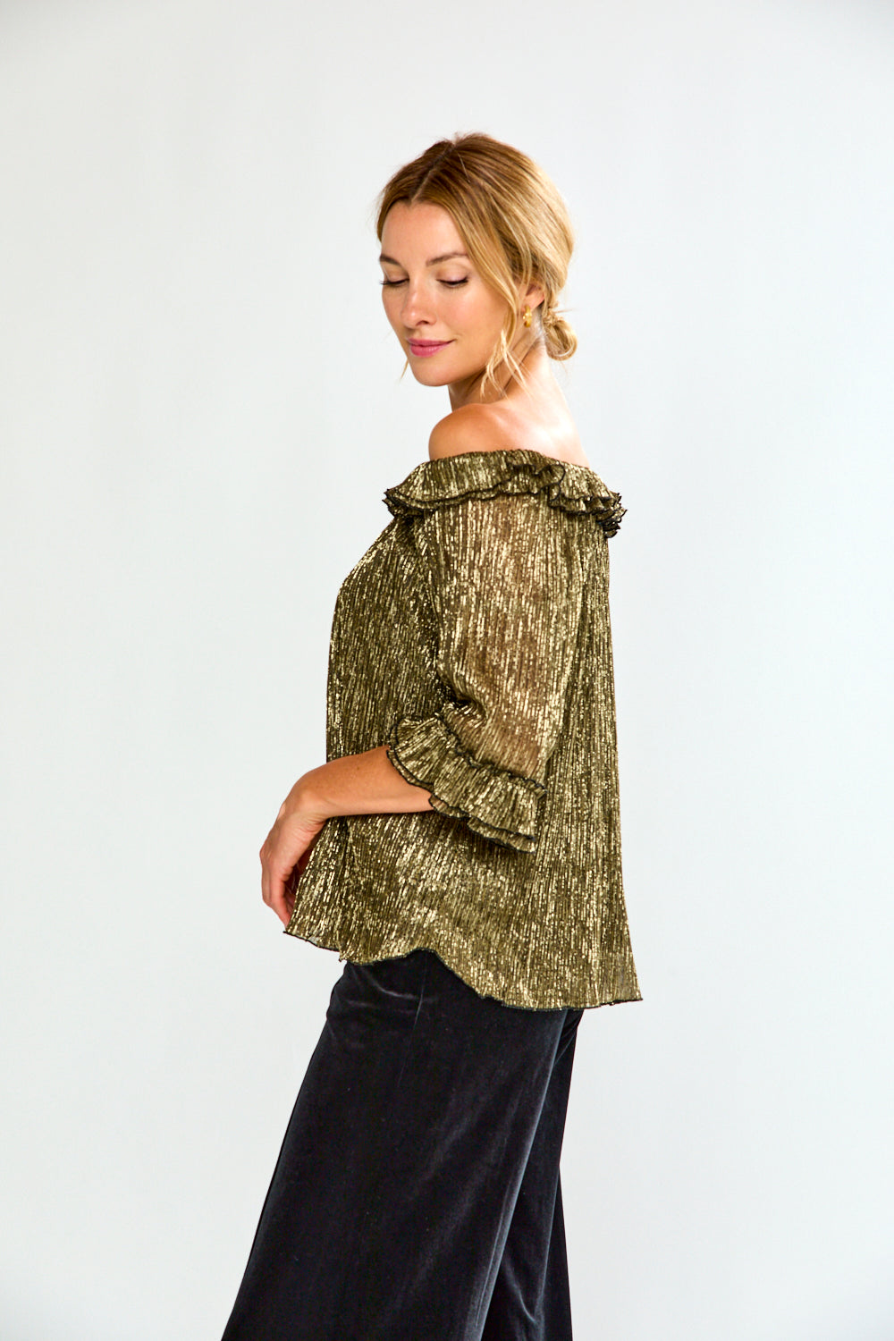 Woman wearing a gold off-shoulder top and black pants on a white background