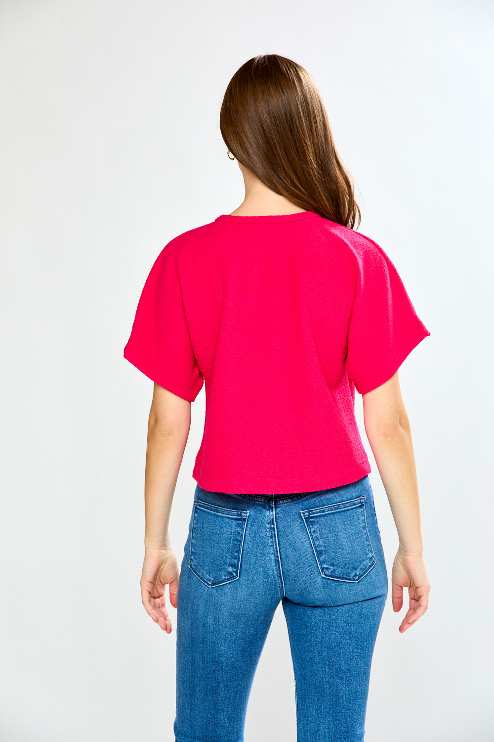 Woman wearing a bright pink top and blue jeans on a white background