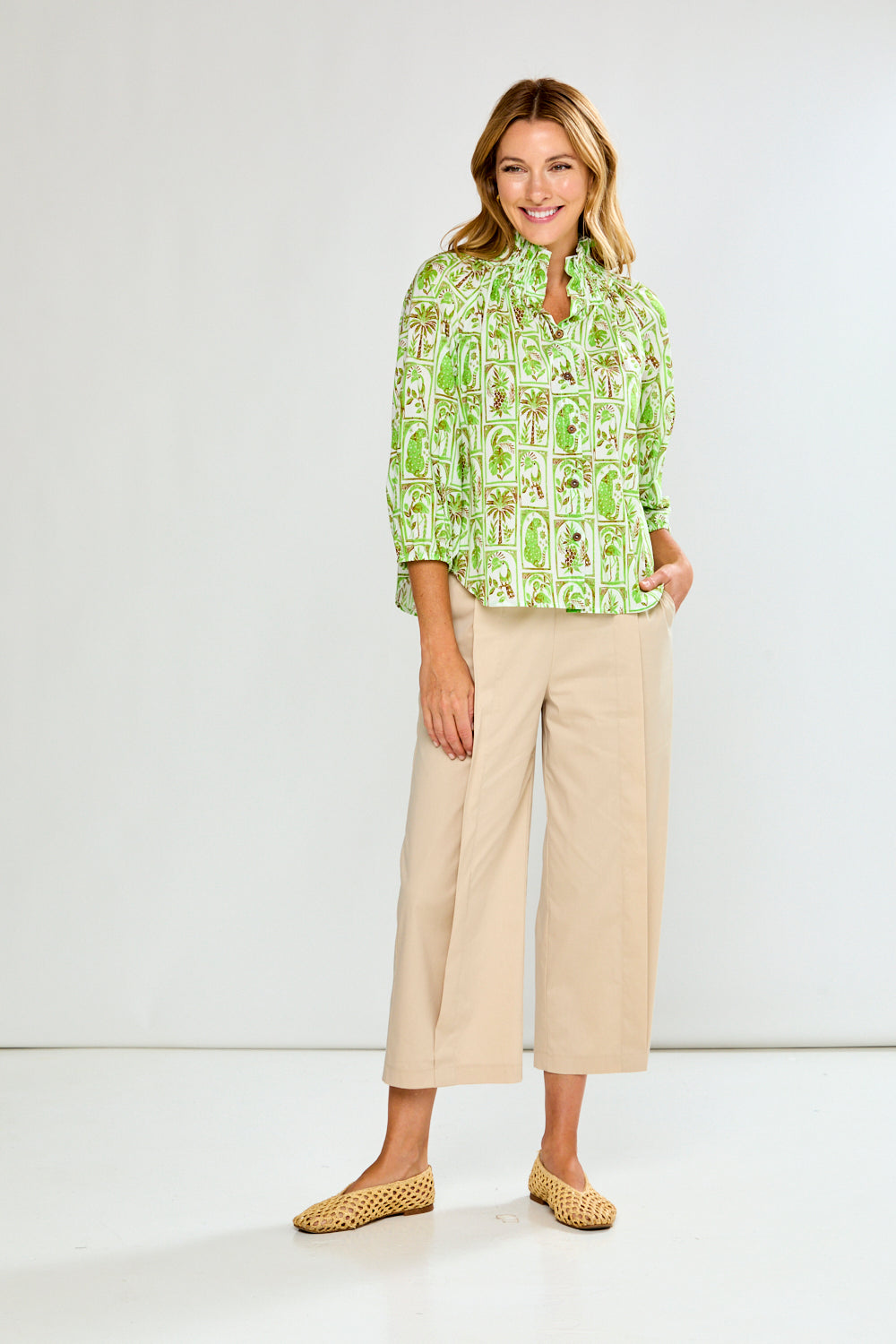 Woman wearing a green patterned blouse and beige pants on a white background