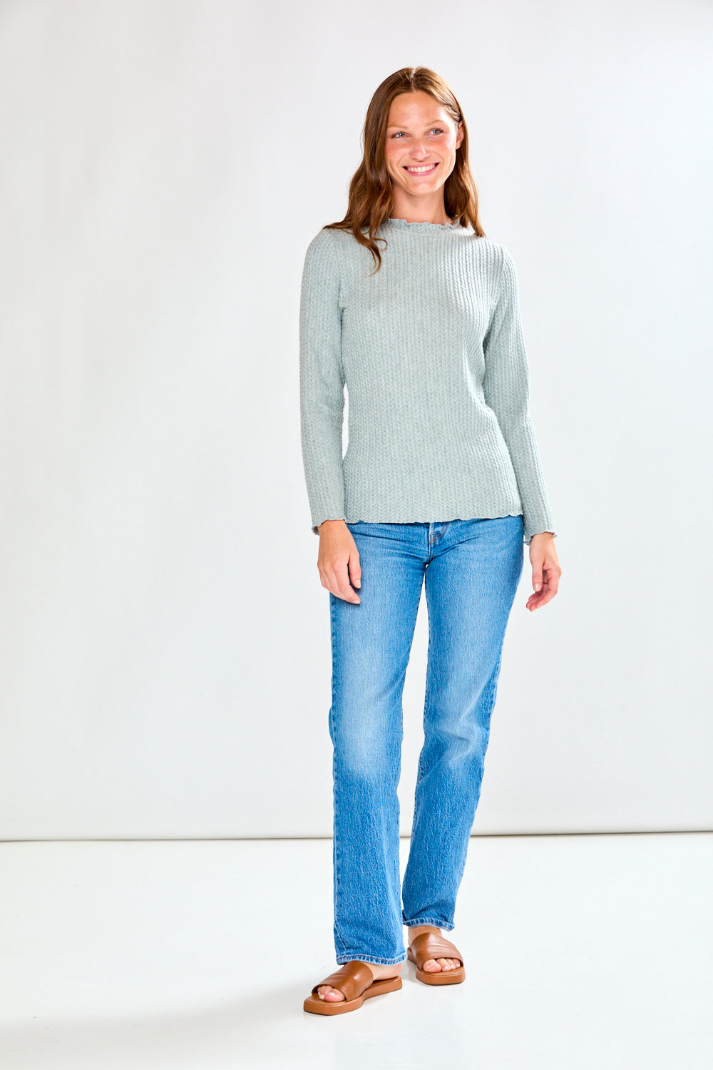 Woman wearing a light grey ribbed shirt and blue jeans on a white background