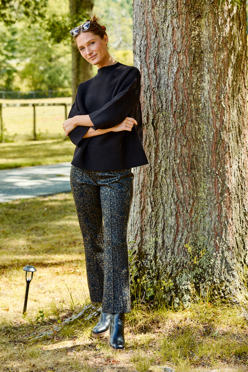 Woman in black outfit leaning against a tree in a park