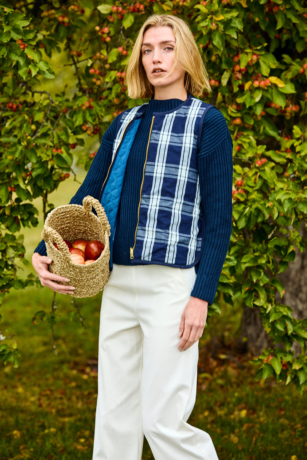 Woman holding a woven basket with apples in an outdoor setting