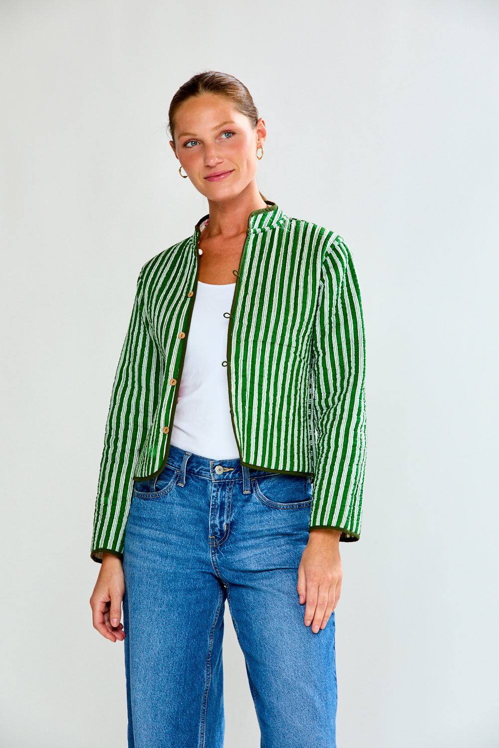 Woman wearing a green and white striped jacket with blue jeans on a plain background