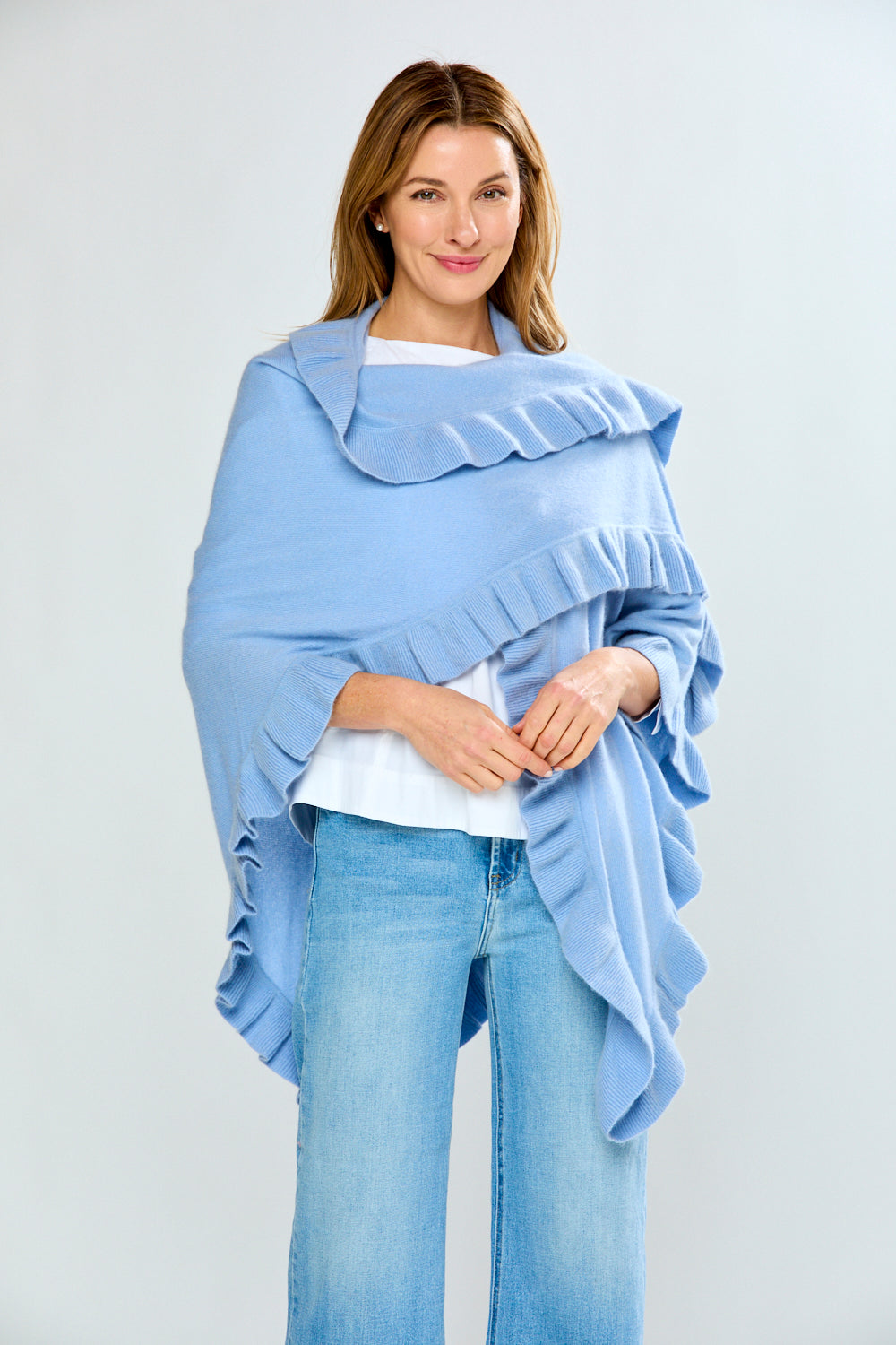 Woman wearing a light blue ruffled shawl over a white top and jeans on a plain background