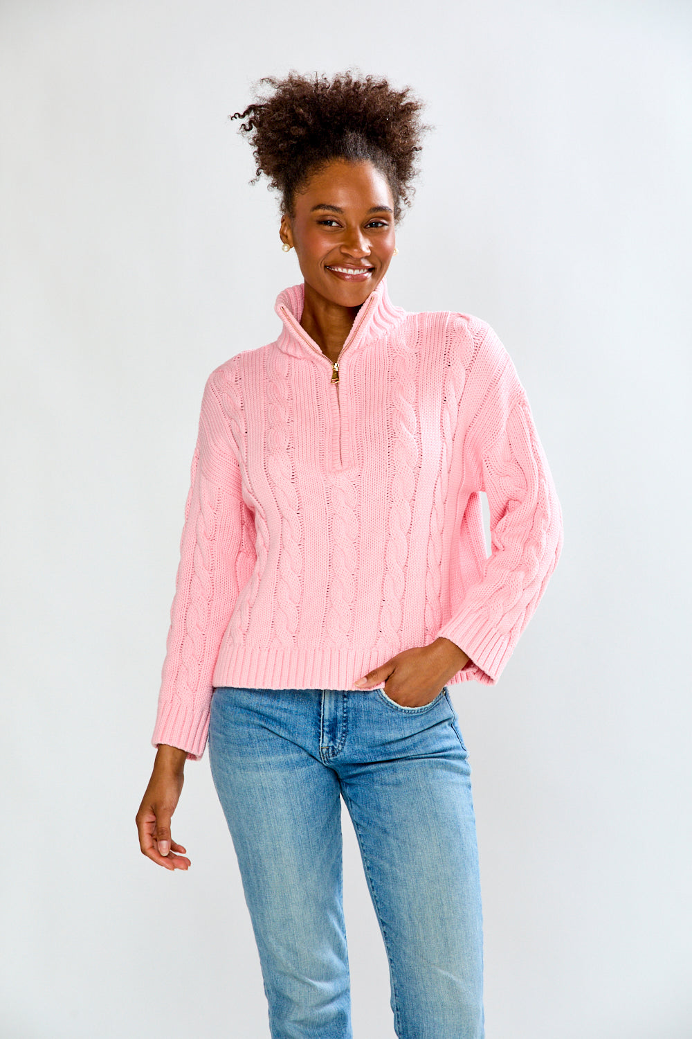 Woman wearing a pink cable knit sweater and blue jeans on a white background
