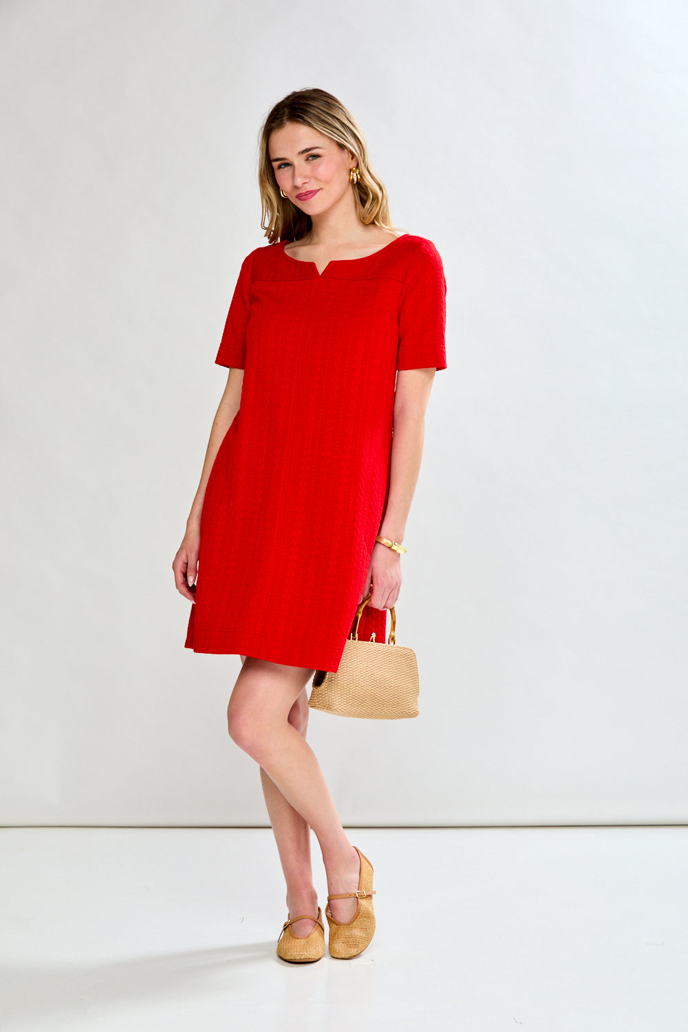 Woman wearing a red dress with a beige handbag on a white background