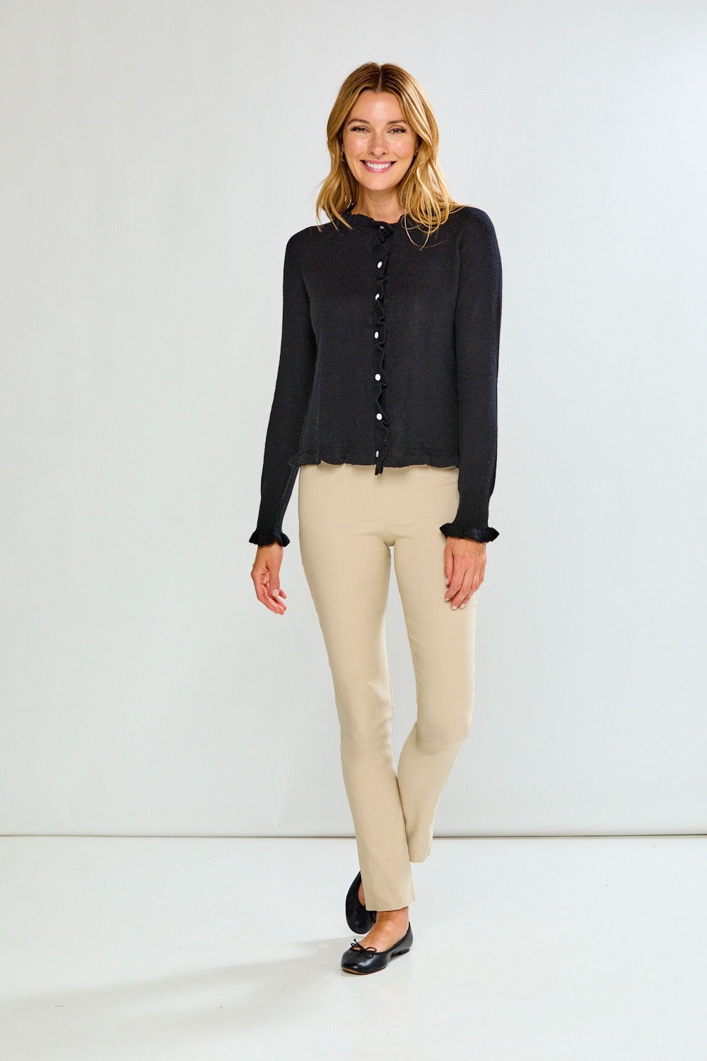 Woman wearing a black button-up sweater and sand pants against a white background