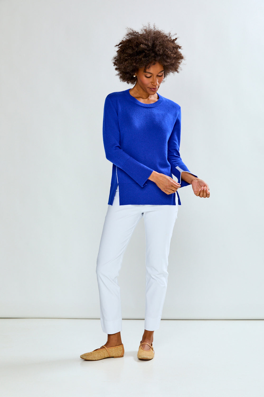 Woman wearing a blue sweater and white pants against a white background