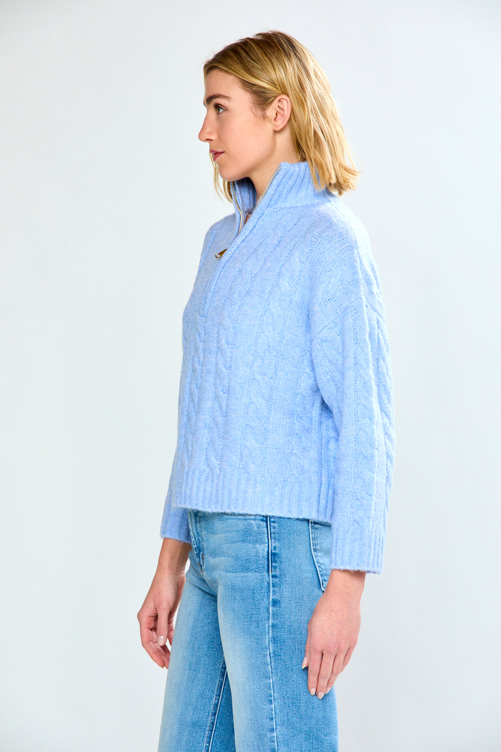 Woman wearing a denim cable knit sweater and blue jeans on a white background