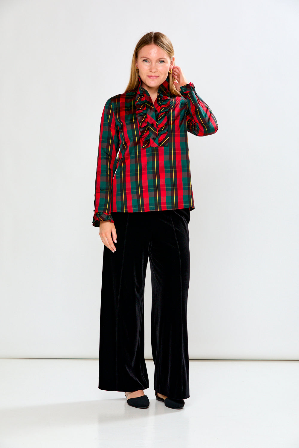 Woman wearing a red and green plaid shirt with a black scarf against a white background