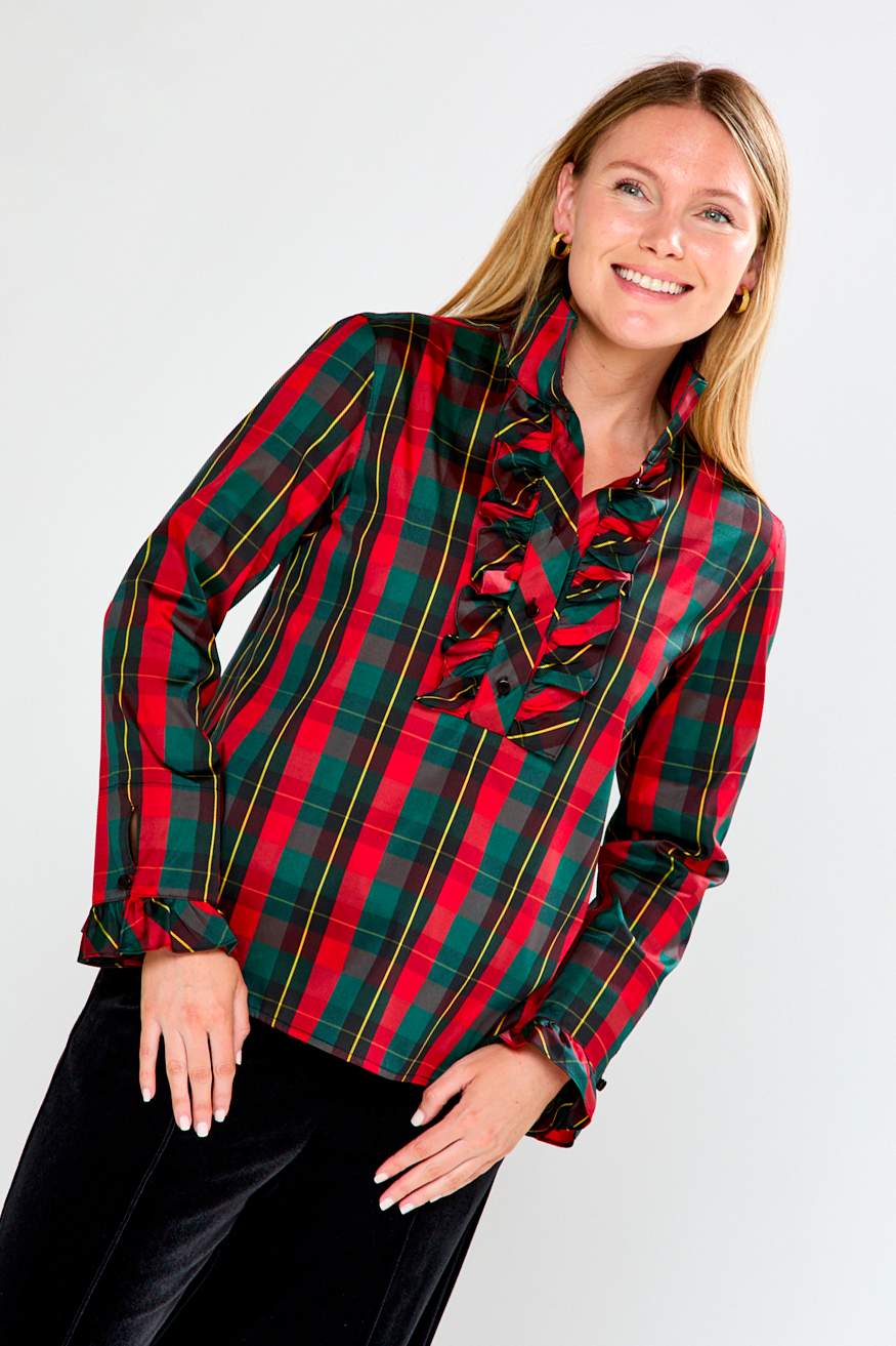 Woman wearing a red and green plaid blouse with ruffles on a white background