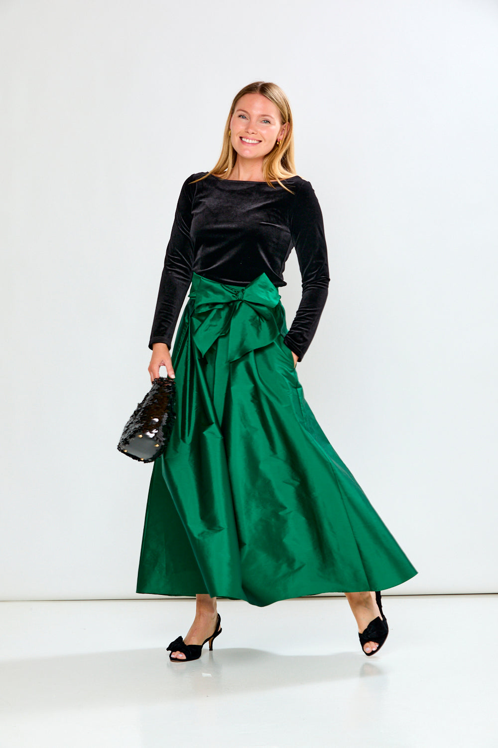 Woman wearing a black top and green skirt with a bow, standing against a white background
