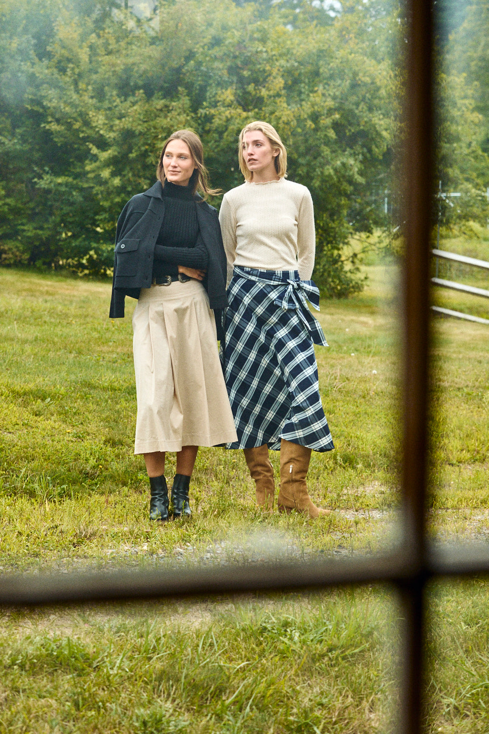 Two women standing in a grassy field with trees in the background