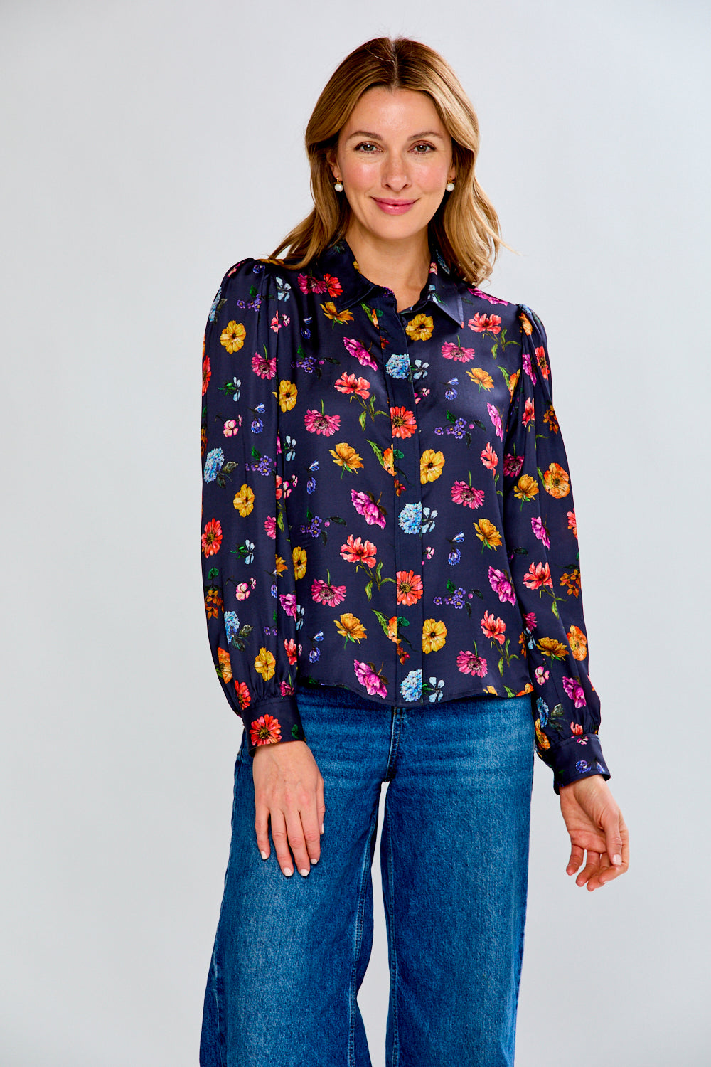 Woman wearing a floral blouse and blue jeans on a plain background
