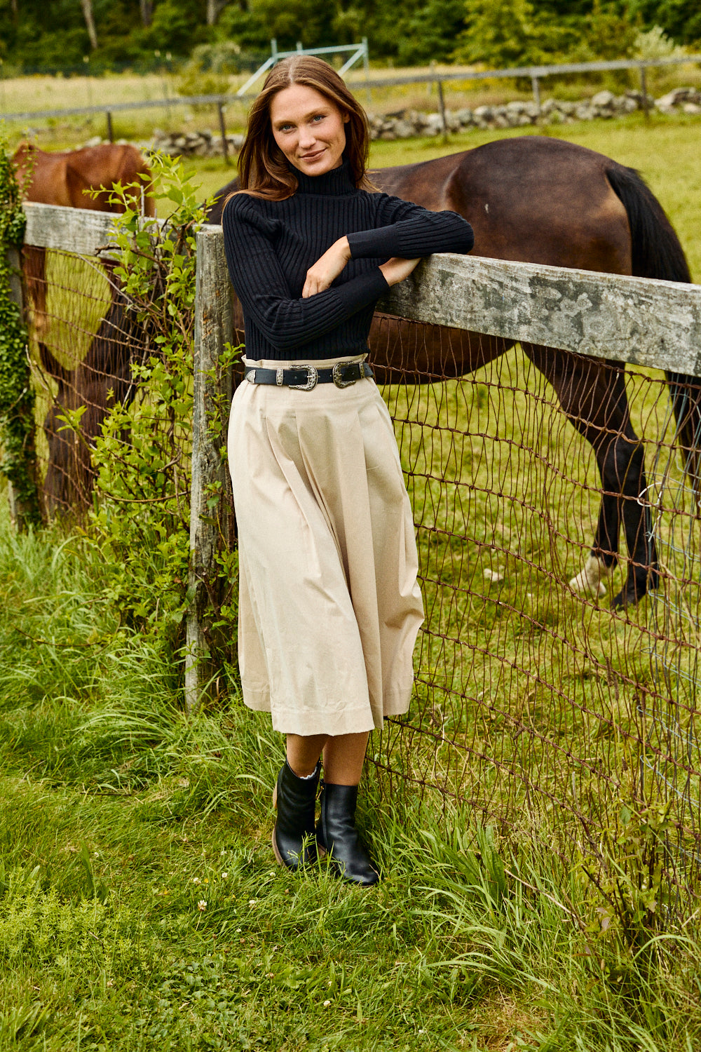 Woman standing next to a horse in a grassy field with a wooden fence.