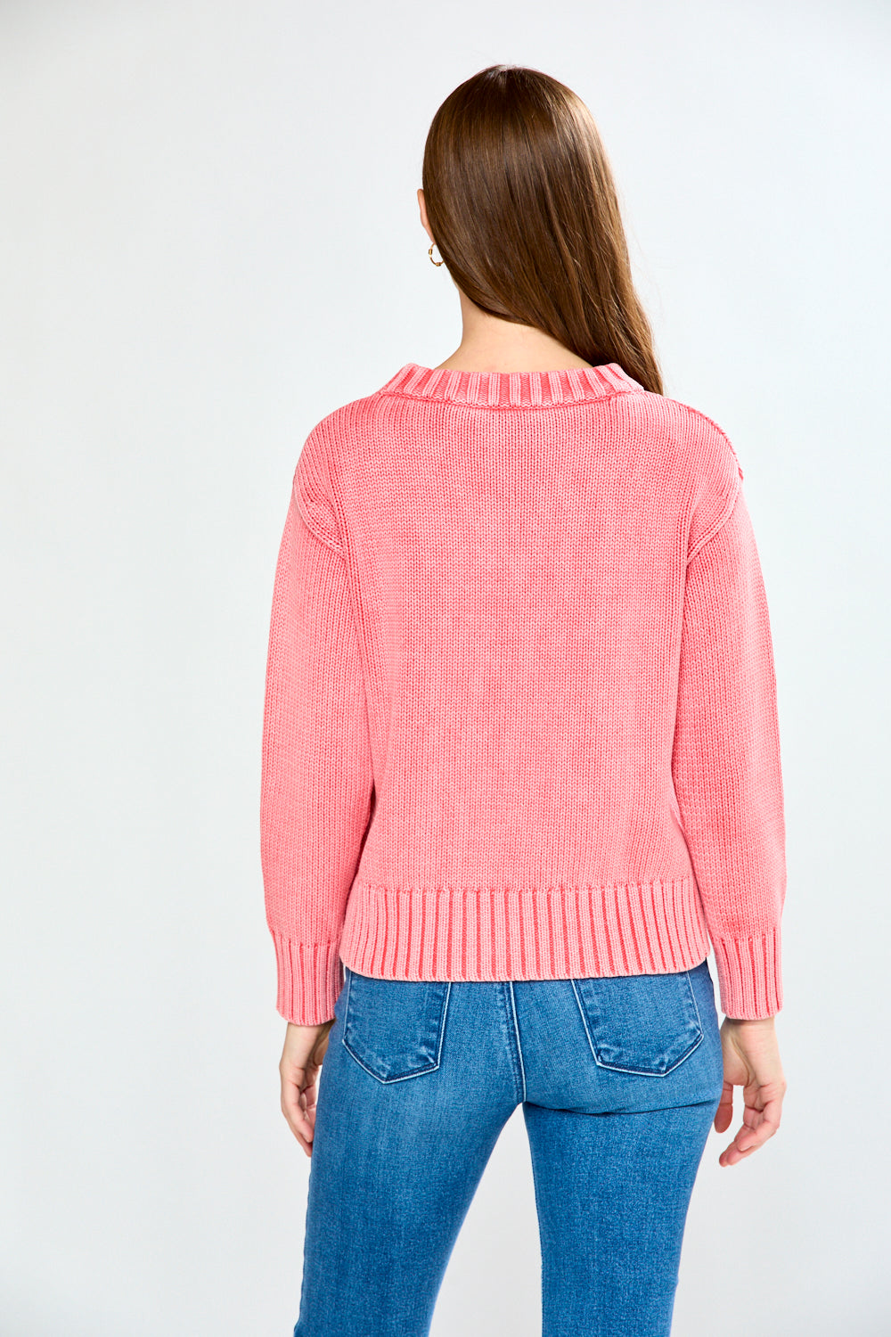 Woman wearing a guava sweater and blue jeans on a white background