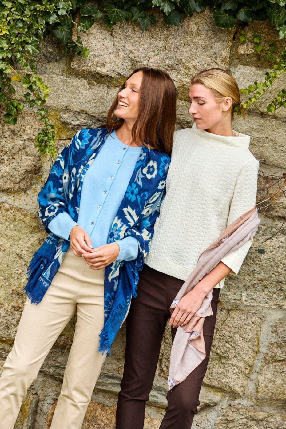 Two women wearing scarves in front of a stone wall