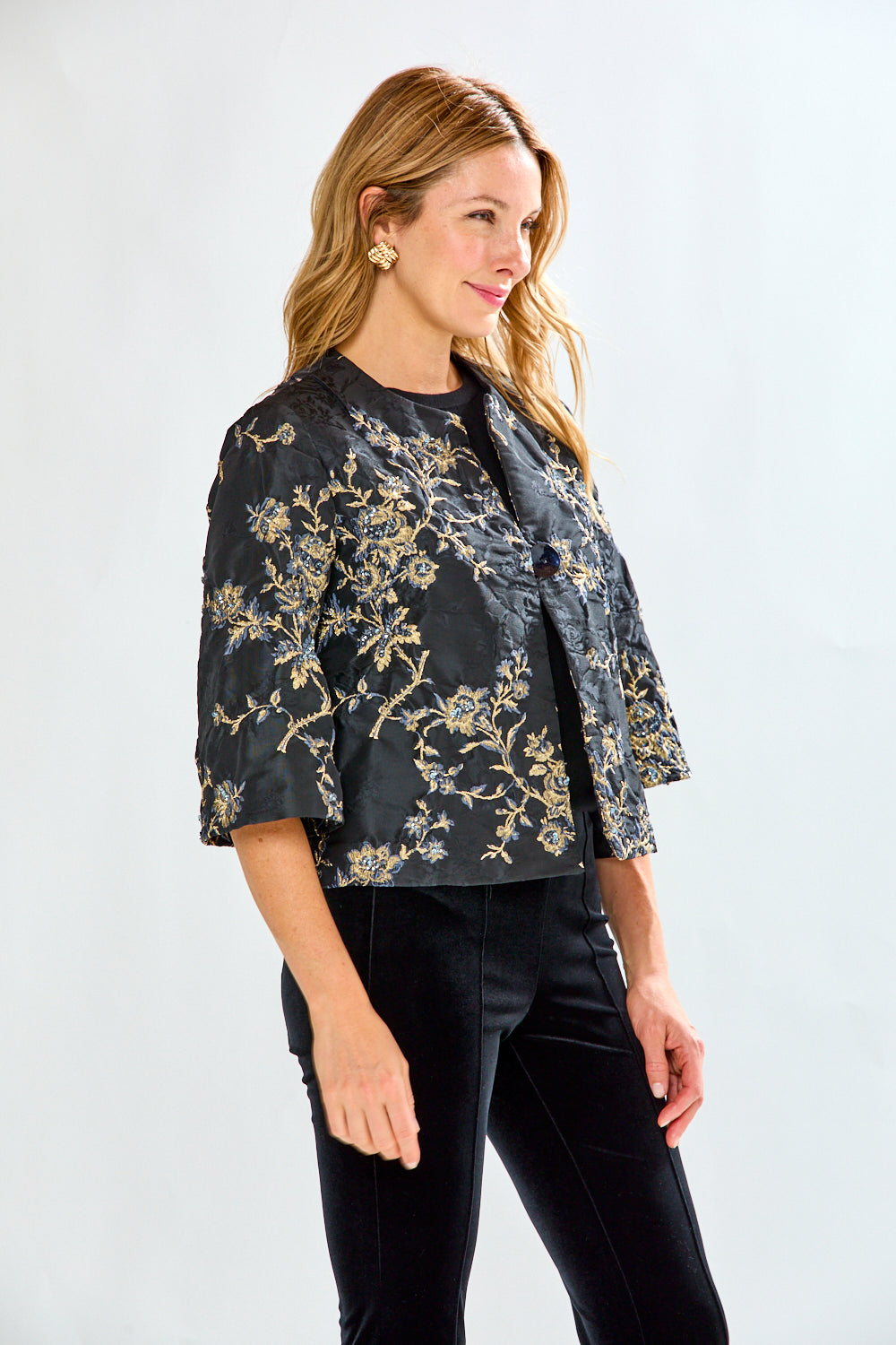 Woman wearing a black floral jacket and black pants on a white background
