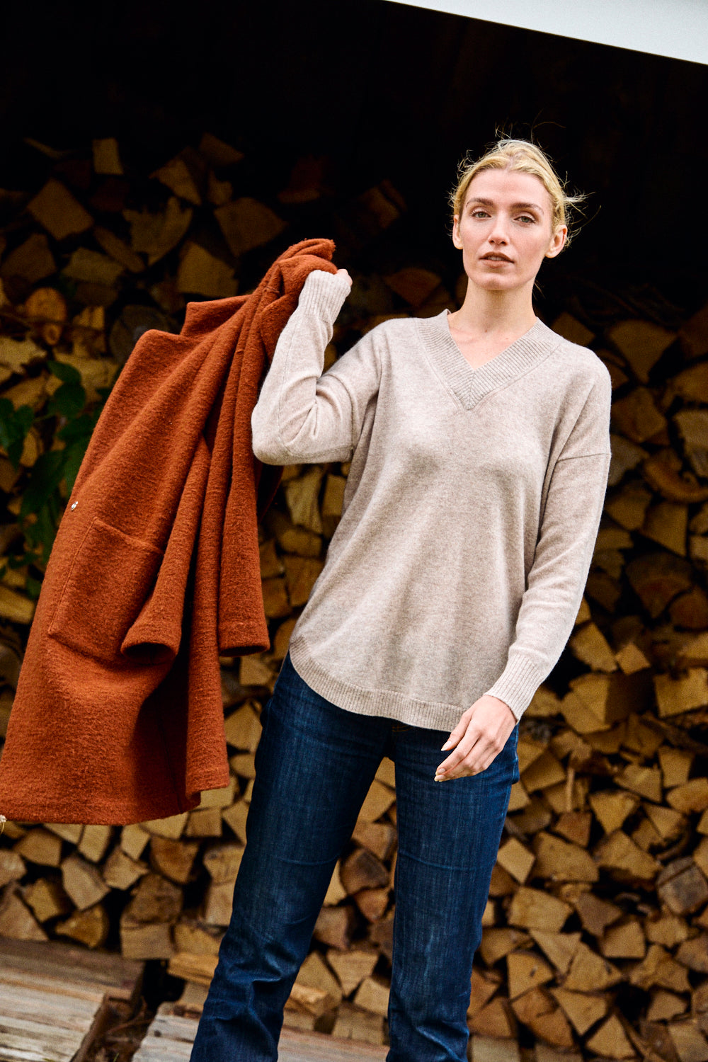 Woman holding a brown coat in front of stacked firewood