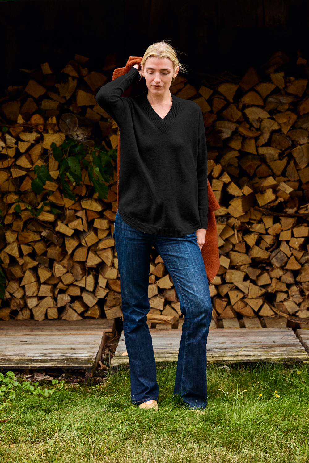 Woman wearing a black sweater in jeans in front of firewood