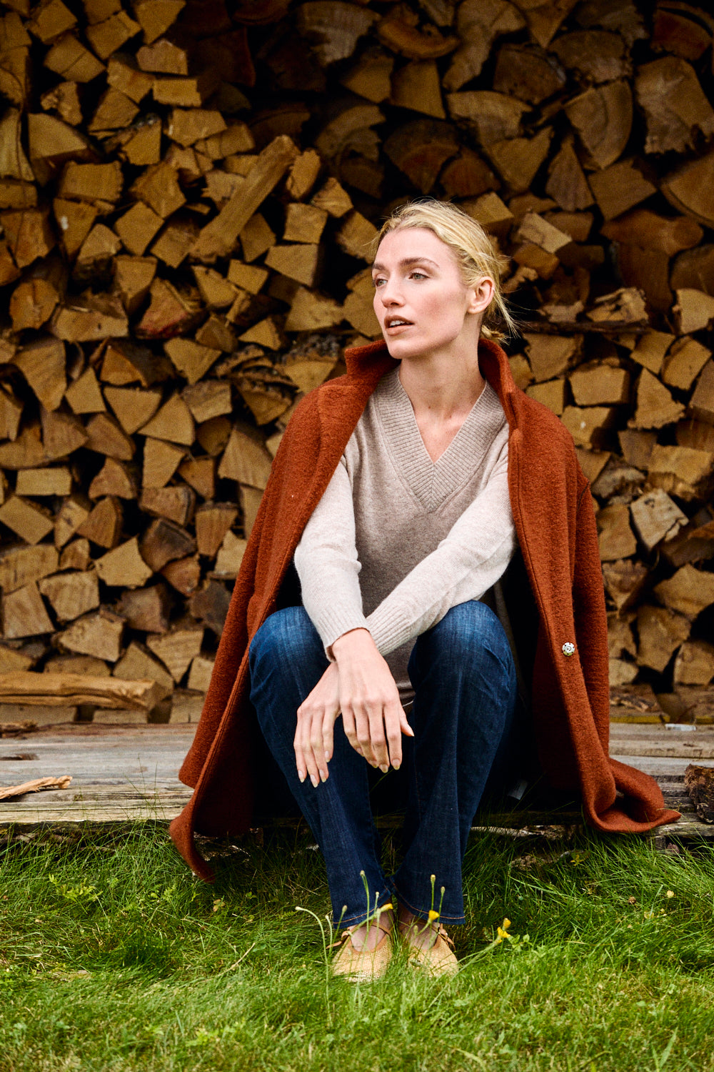 Woman sitting in front of stacked firewood wearing a red coat.