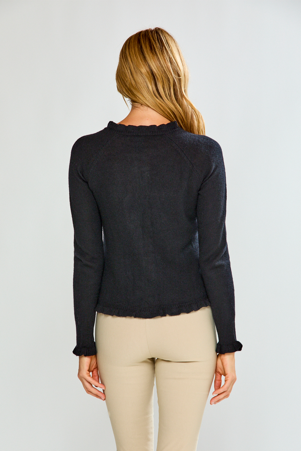 Woman wearing a black button-up sweater and sand pants against a white background