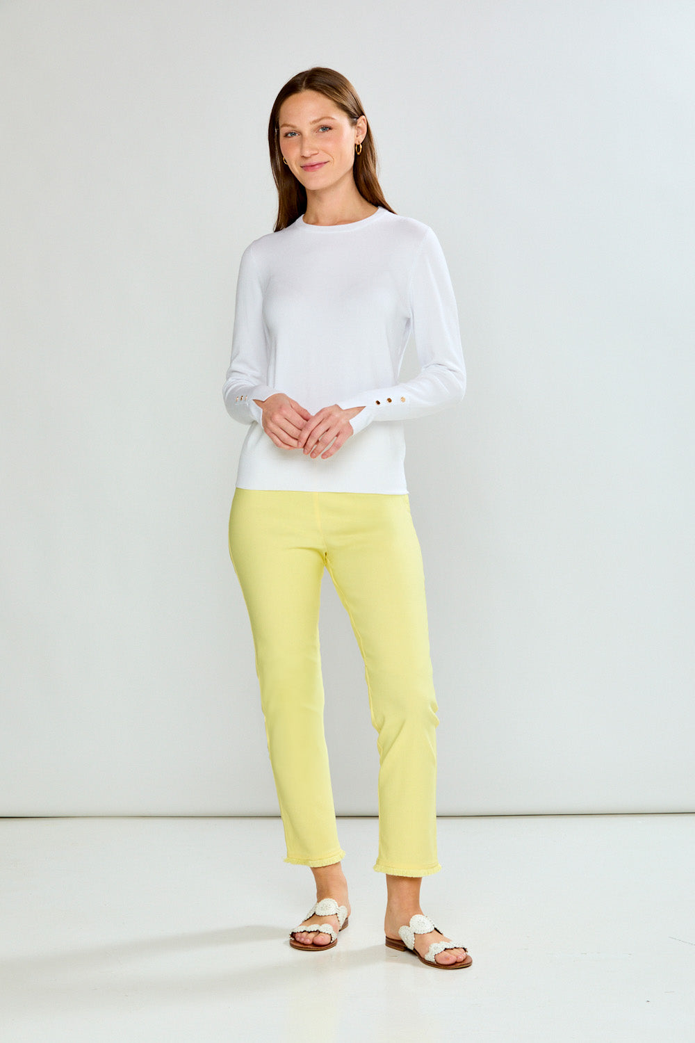 Woman wearing a white long-sleeve sweater and yellow pants on a light gray background