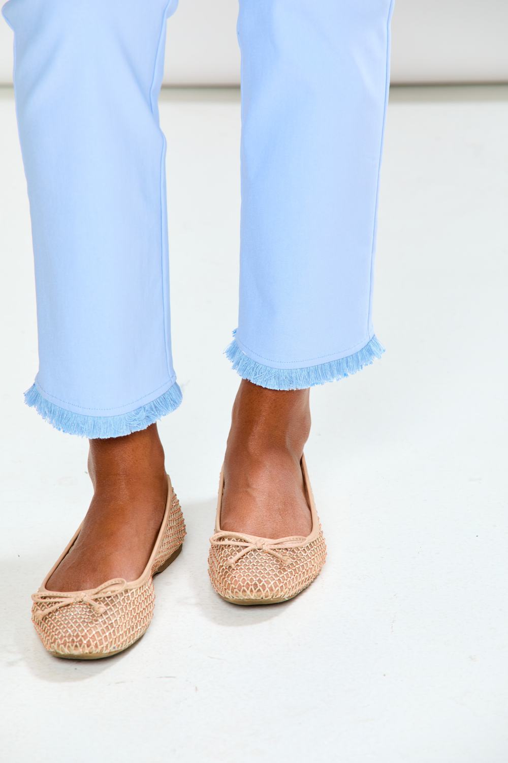 Person wearing light blue jeans and woven shoes on a white background