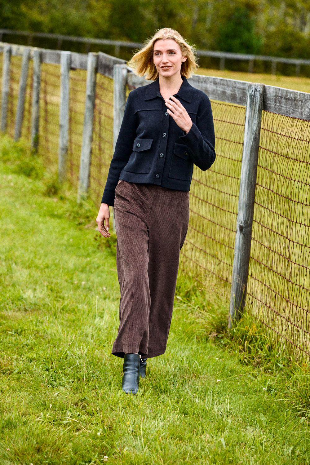 Woman standing in a grassy field next to a wooden fence