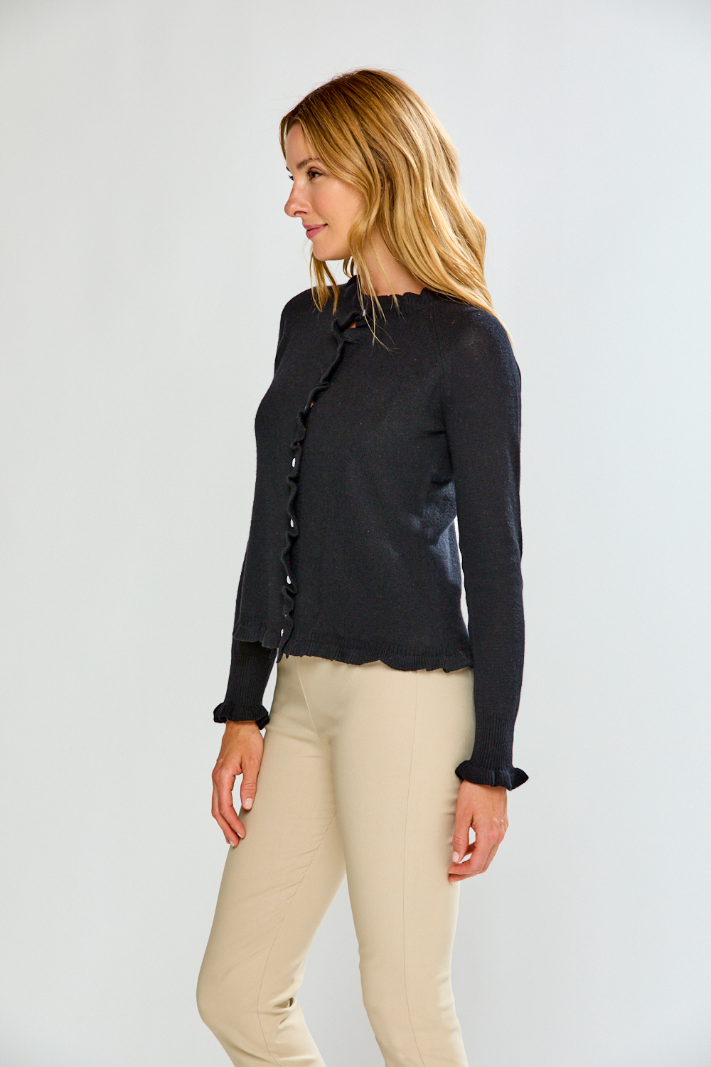 Woman wearing a black button-up sweater and sand pants against a white background