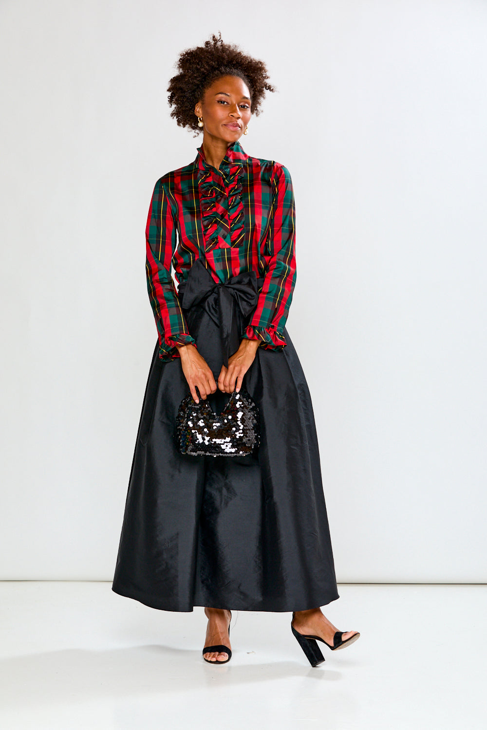 Woman wearing a plaid shirt and black skirt with a sequin bag on a white background